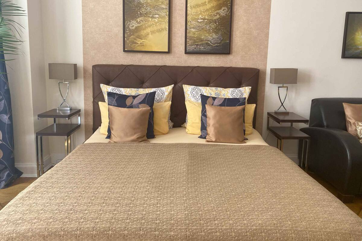 Une chambre d  ’hôtel avec un grand lit, deux tables de chevet, un canapé en cuir noir et deux œuvres d’art encadrées accrochées au mur.