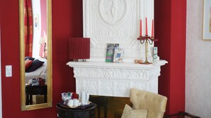 A room with a red wall, a white fireplace with red candles, a mirror, and a chair. - mittendrin - Boutique Hotel Berlin (Berlin)