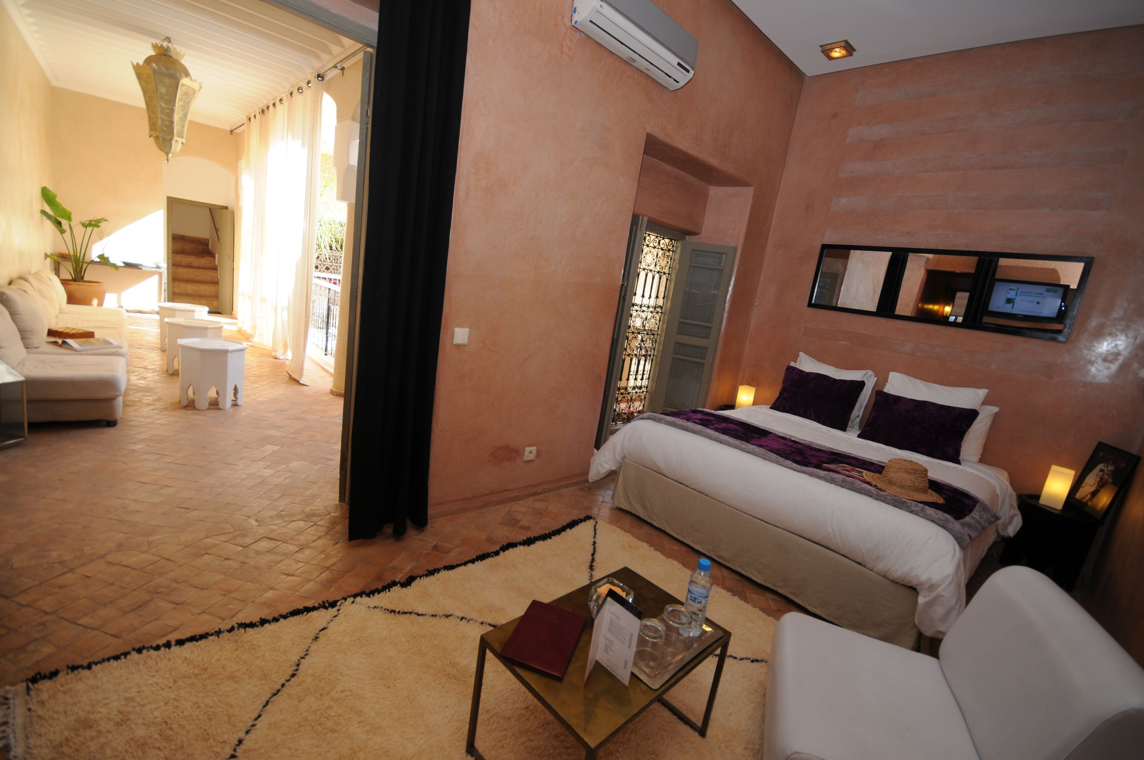 Habitación de hotel con cama, zona de estar con sofá y una mesita, planta en maceta y una escalera que da a un espacio exterior.
