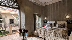 Een slaapkamer met een groot bed, een klein tafeltje met een bloevas en uitzicht op een binnenplaats.