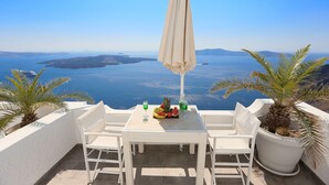 A white table with two chairs and an umbrella, overlooking a scenic view of the sea and islands. - Kafieris Blue  (Santorini)
