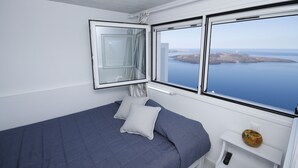 A bedroom with a bed, a window with a view of the sea, and a small shelf with a vase. - Kafieris Blue  (Santorini)