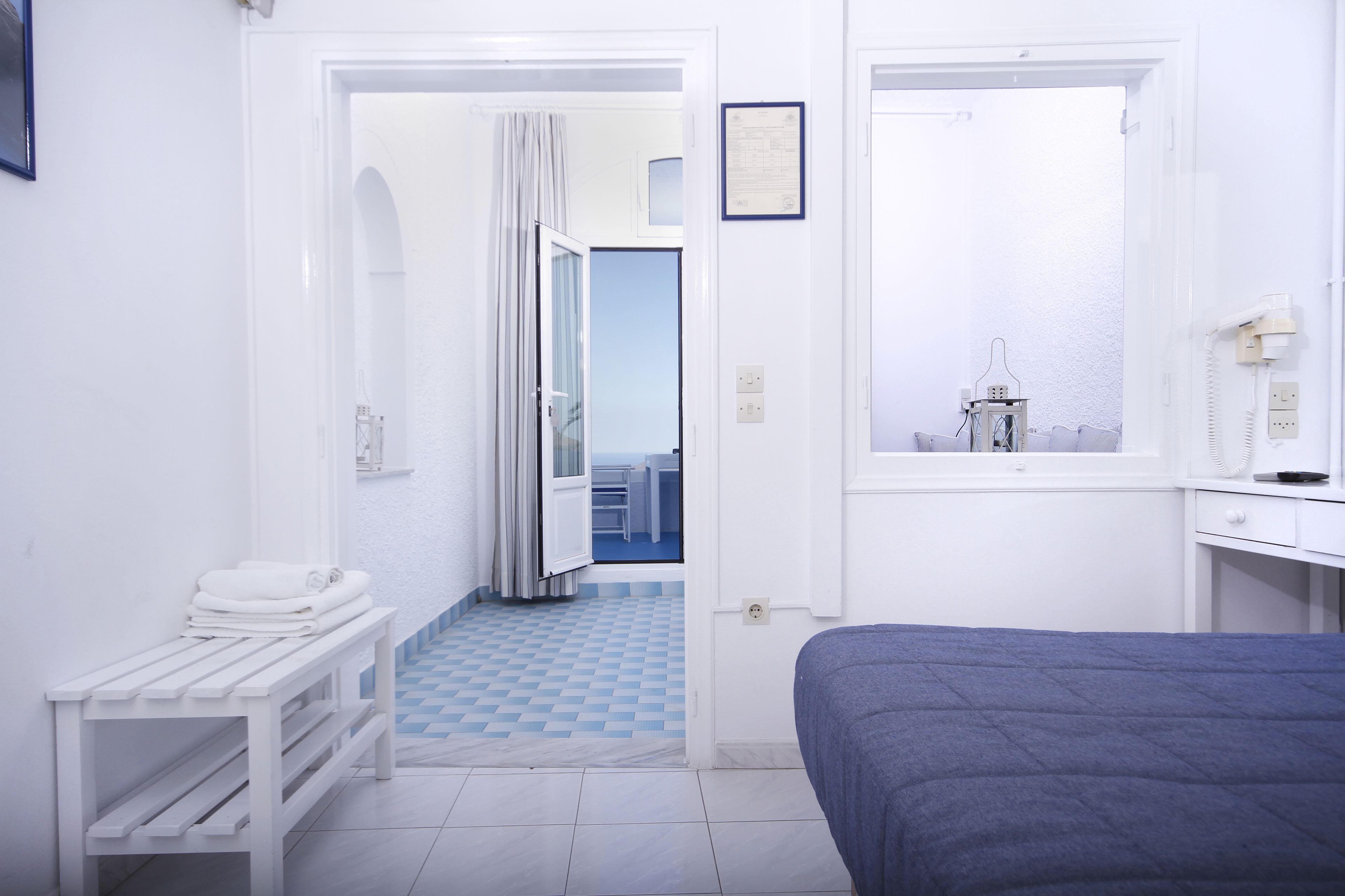 A hotel room with a bed, a bench with towels, a window, and a door leading to a balcony.