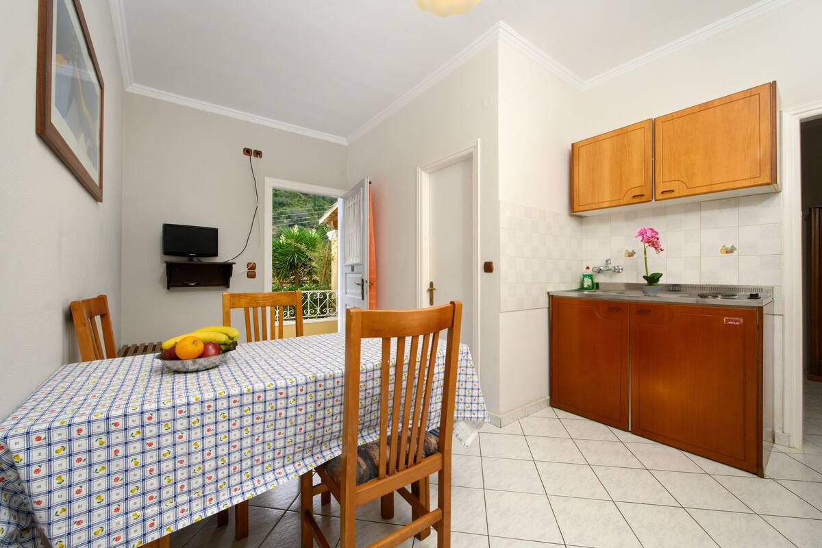 A dining area with a table set for four, a kitchen with wooden cabinets, and a view of greenery outside.