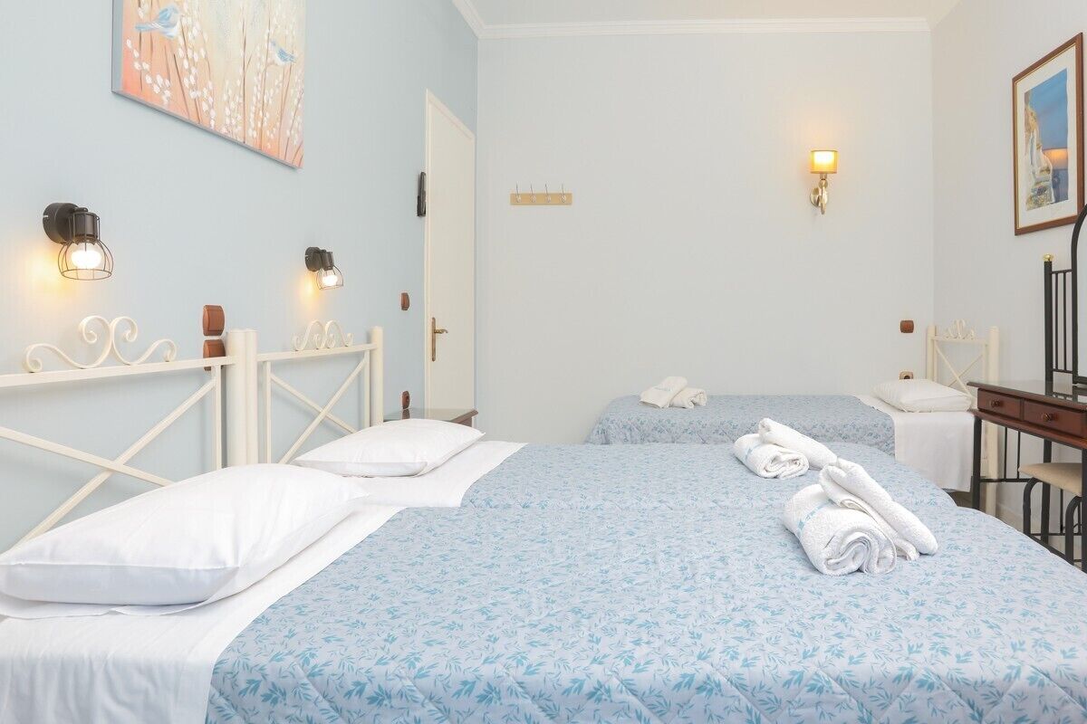 A hotel room with two beds, a desk, and a chair. There are wall-mounted lights and a painting on the wall.
