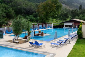 A pool area with lounge chairs and umbrellas, surrounded by greenery and a building in the background. - Marina Apartments (Corfu)