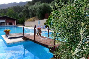 A pool area with a wooden deck, lounge chairs, and a potted plant. - Marina Apartments (Corfu)