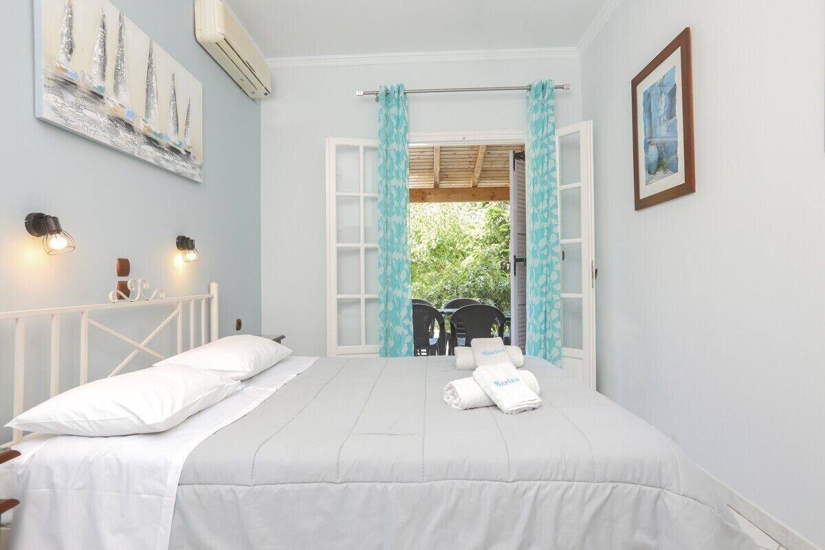 A bedroom with a bed, white curtains, a window, and a painting on the wall.