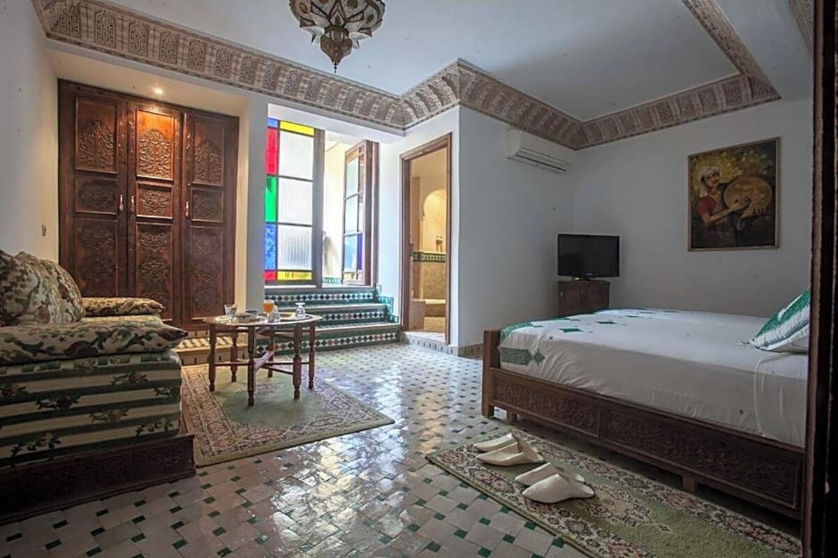 A room with a bed, a sofa, a TV, a patterned floor, and a door leading to another room.