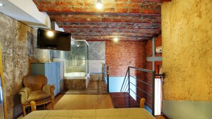 A hotel room with a bed, a chair, a television, a shower, and a staircase. - La Fresque Hotel (Buenos Aires)