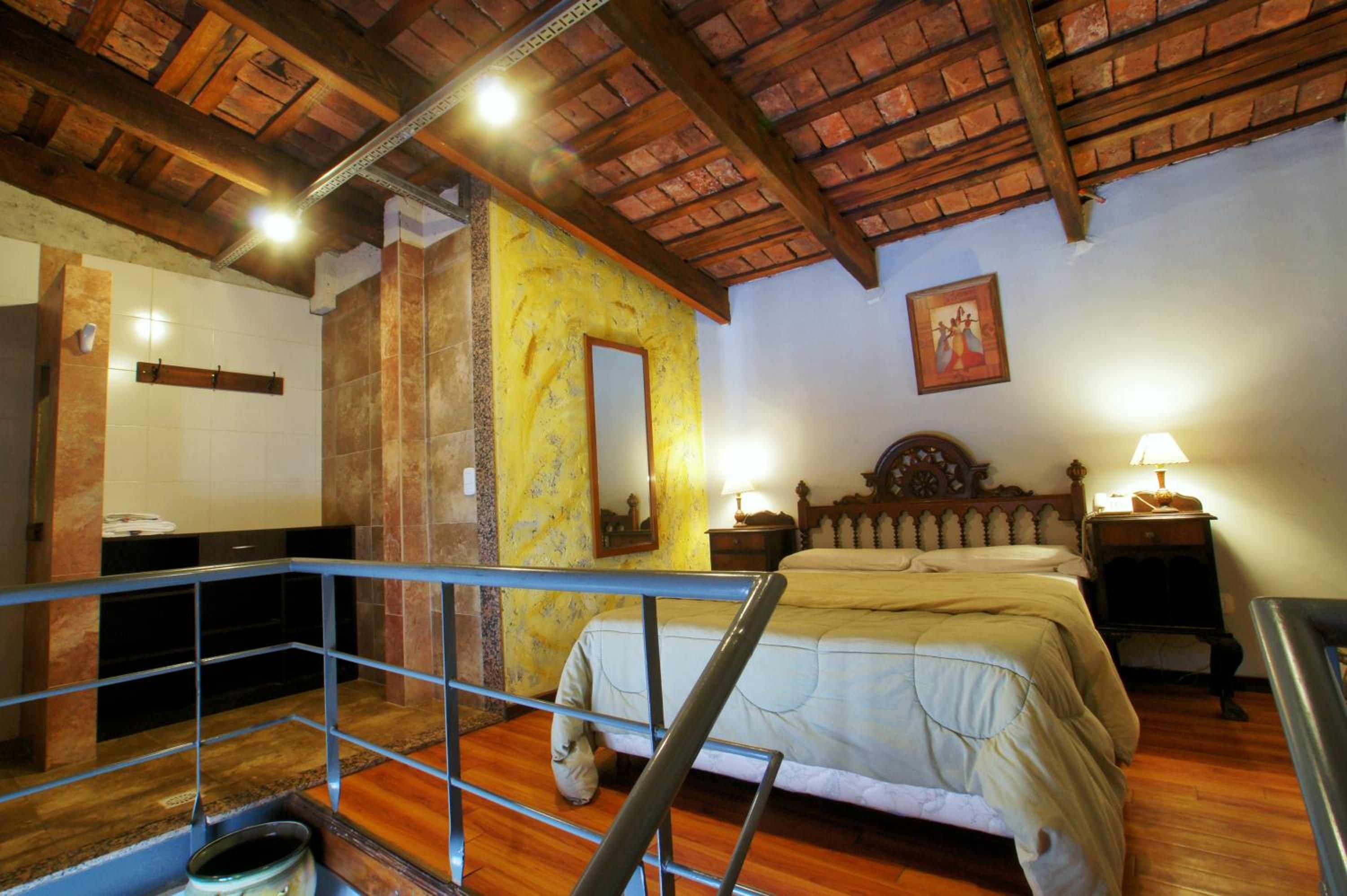 A bedroom with a bed, a wooden headboard, a nightstand, a lamp, a mirror, and a bathroom with a shower.