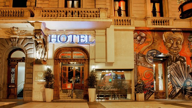 A hotel facade with a prominent neon sign, ornate architectural details, and a mural on the right side. - La Fresque Hotel (Buenos Aires)