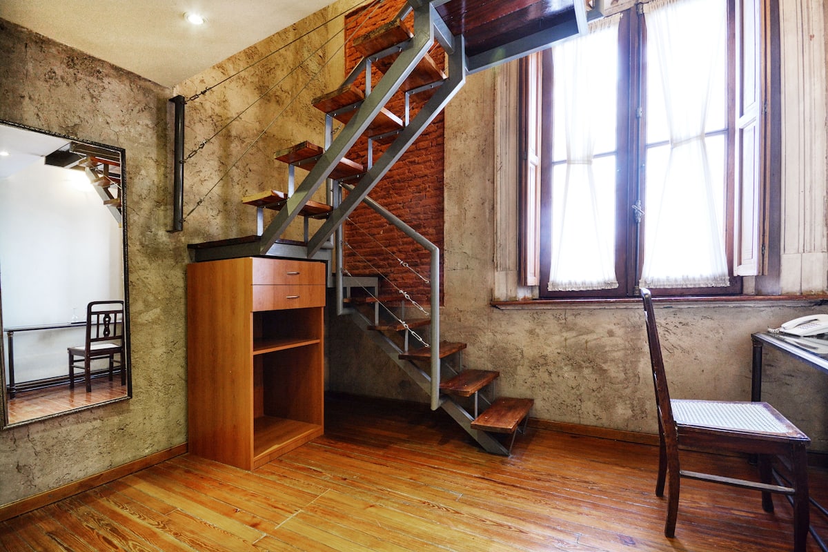 A room with a wooden floor, a metal staircase, a wooden desk, and a chair.