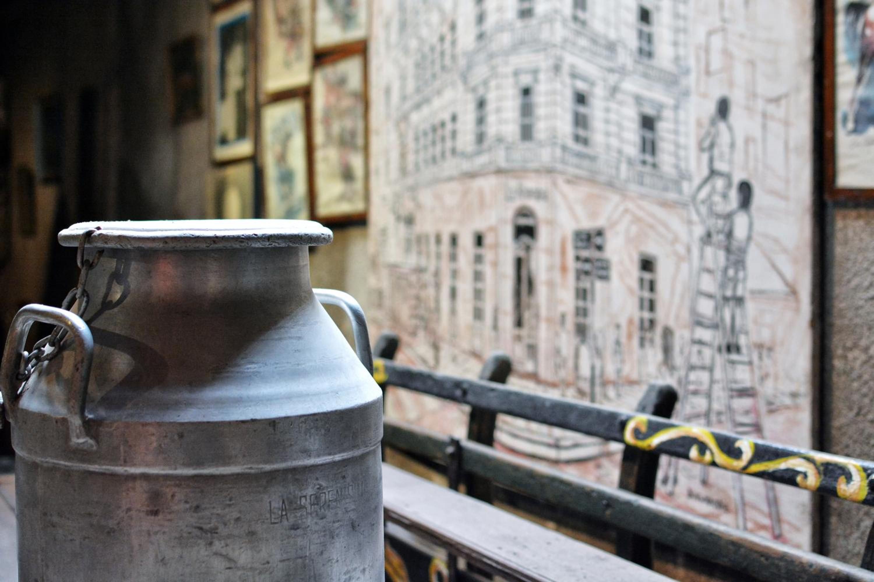 A metal container with handles, possibly a kettle, in front of a wall with a mural.