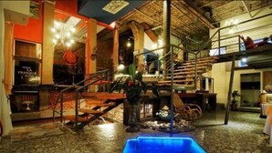 A spacious indoor area with a stone floor, a blue pool, wooden furniture, and a staircase. - La Fresque Hotel (Buenos Aires)