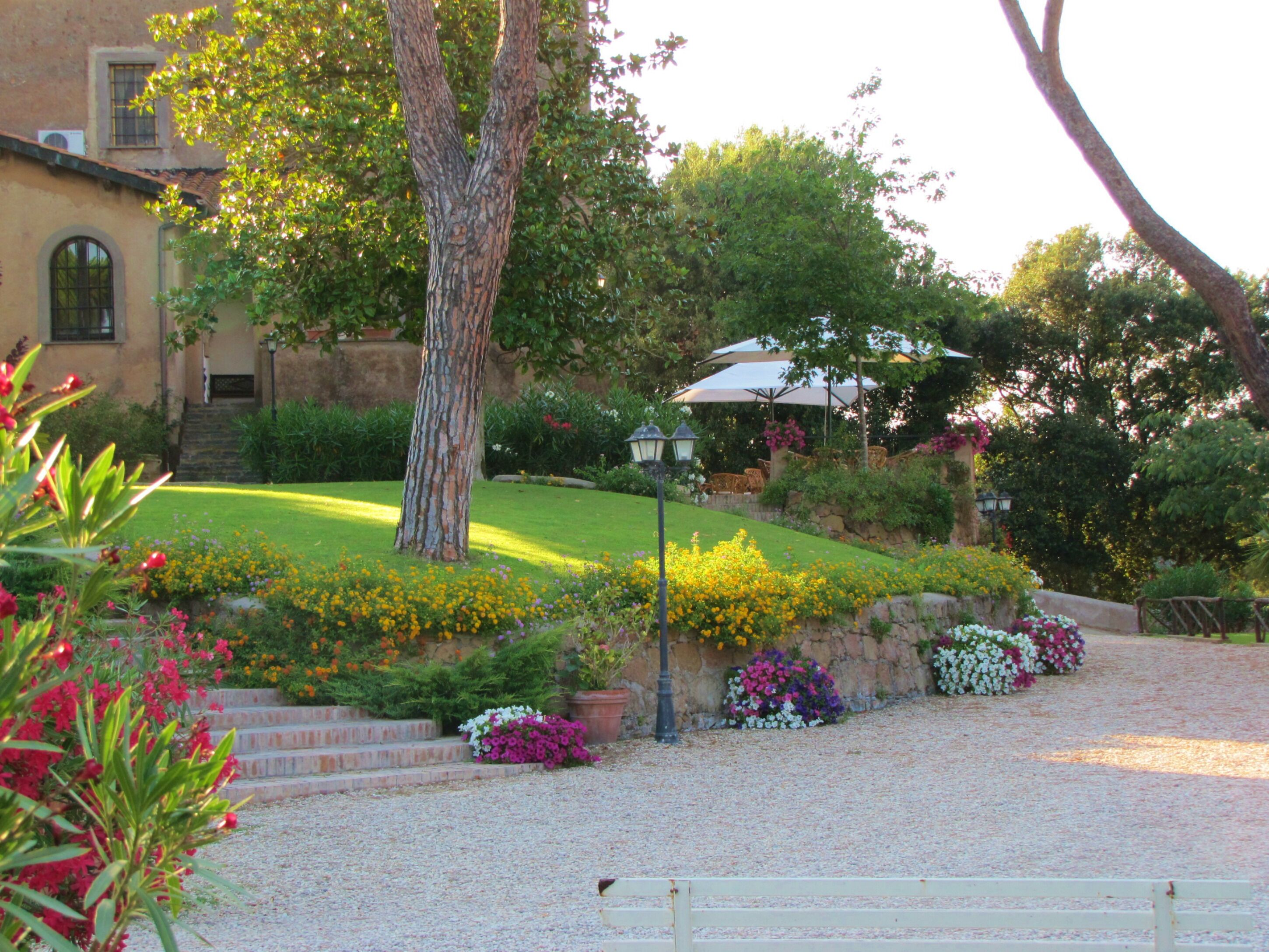 Un jardin avec un chemin de gravier, un banc et un bâtiment doté d’une fenêtre et d’un escalier.