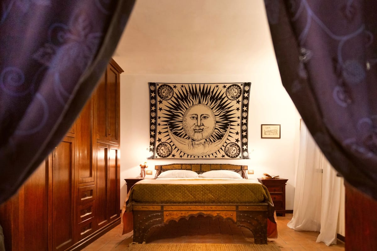A bedroom with a bed, wooden wardrobe, and a large tapestry on the wall.