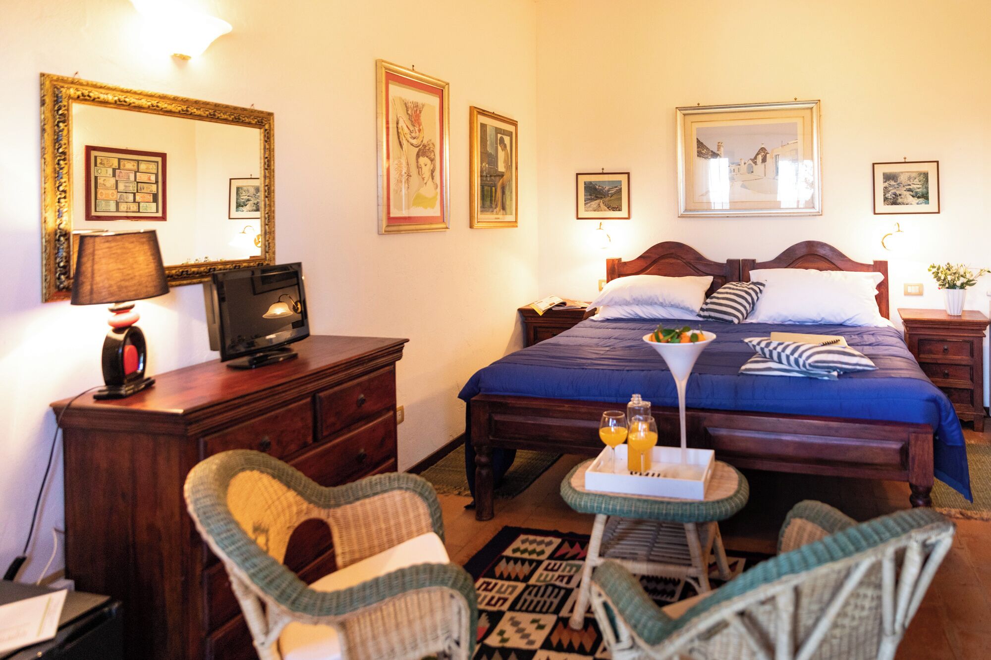 Una camera d'albergo con un letto, due comodini, una scrivania con una lampada, una sedia e un tavolino con un vassoio di bevande.