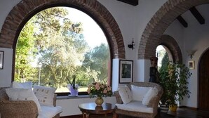 Una habitación con dos sofás de mimbre, una mesita redonda pequeña y un ventanal arqueado grande con vistas a la vegetación.