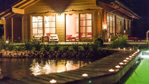 Una casa de madera con piscina y zona de estar exterior, iluminada por velas.