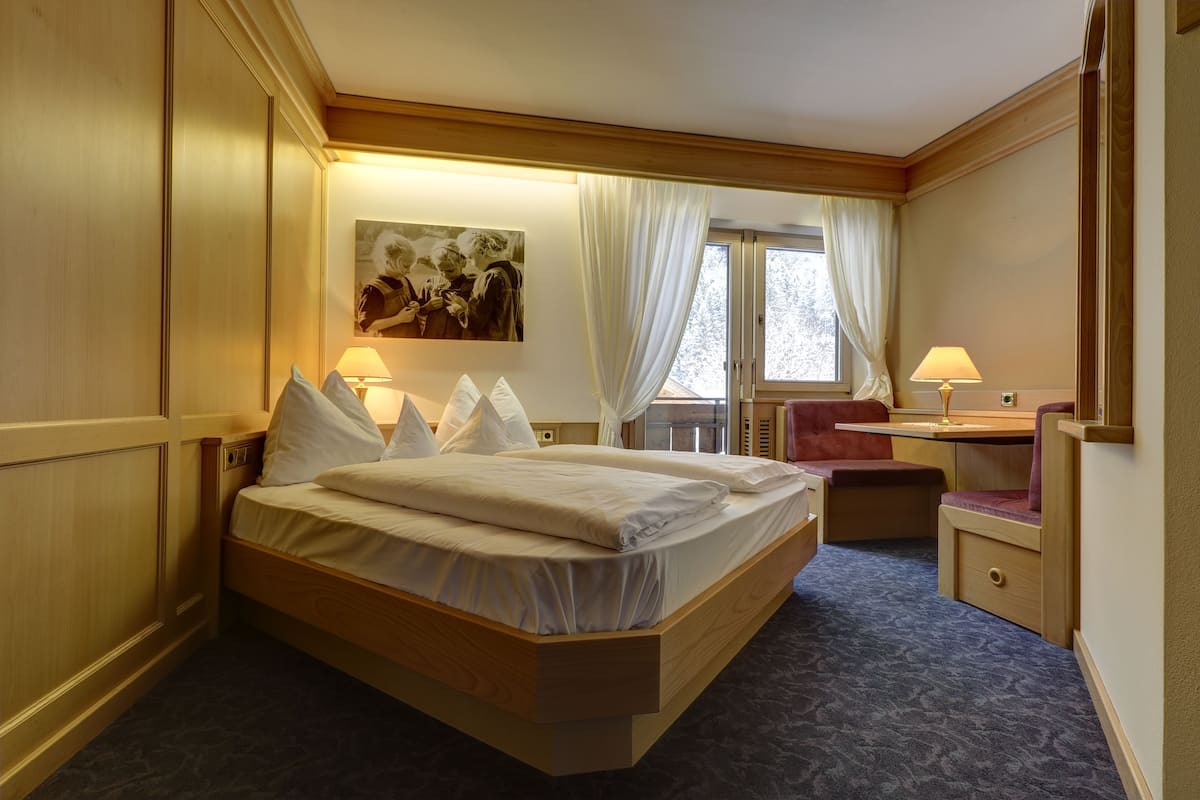 A hotel room with a wooden bed, a desk, a chair, and a window with curtains.