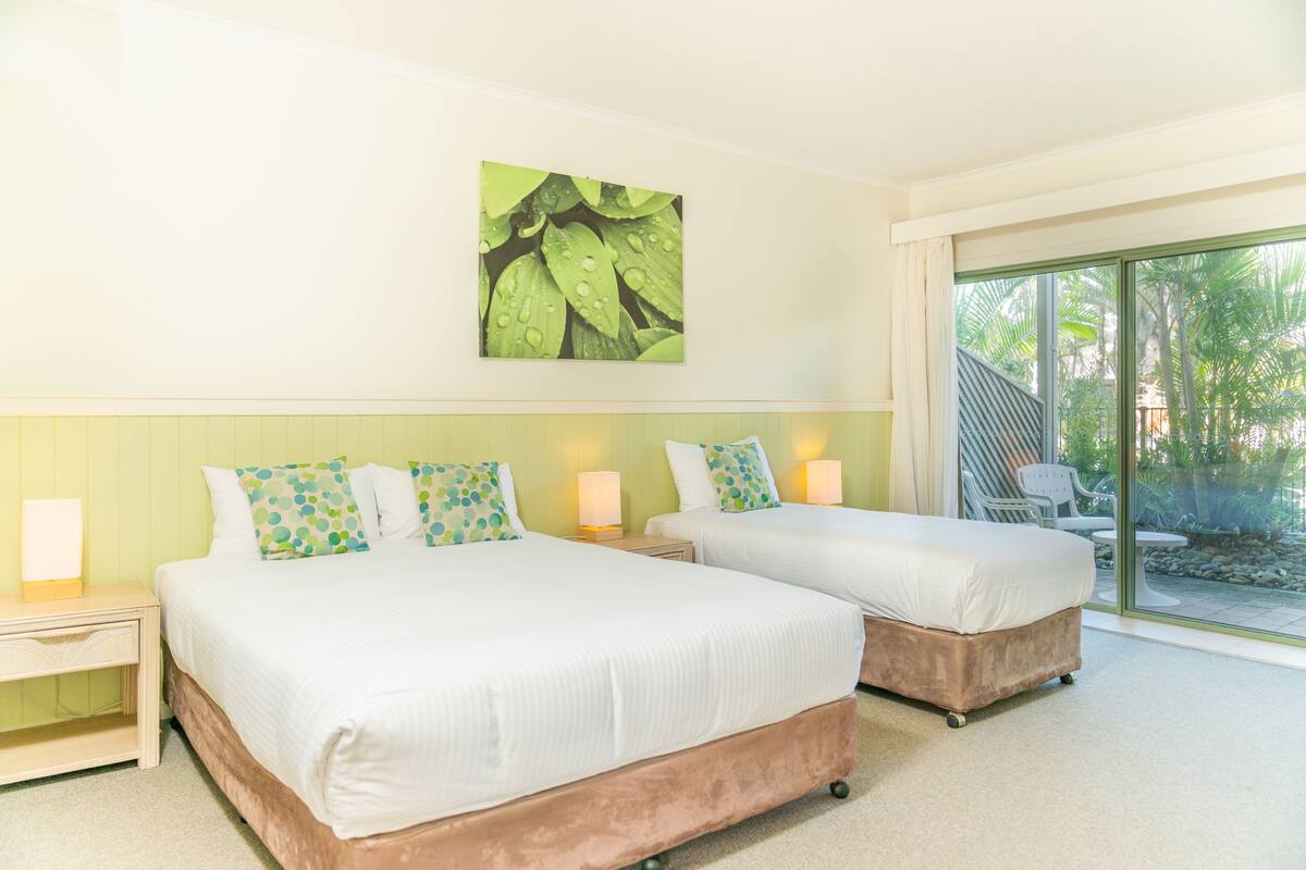 A hotel room with two beds, a large window, and a view of the outdoors.