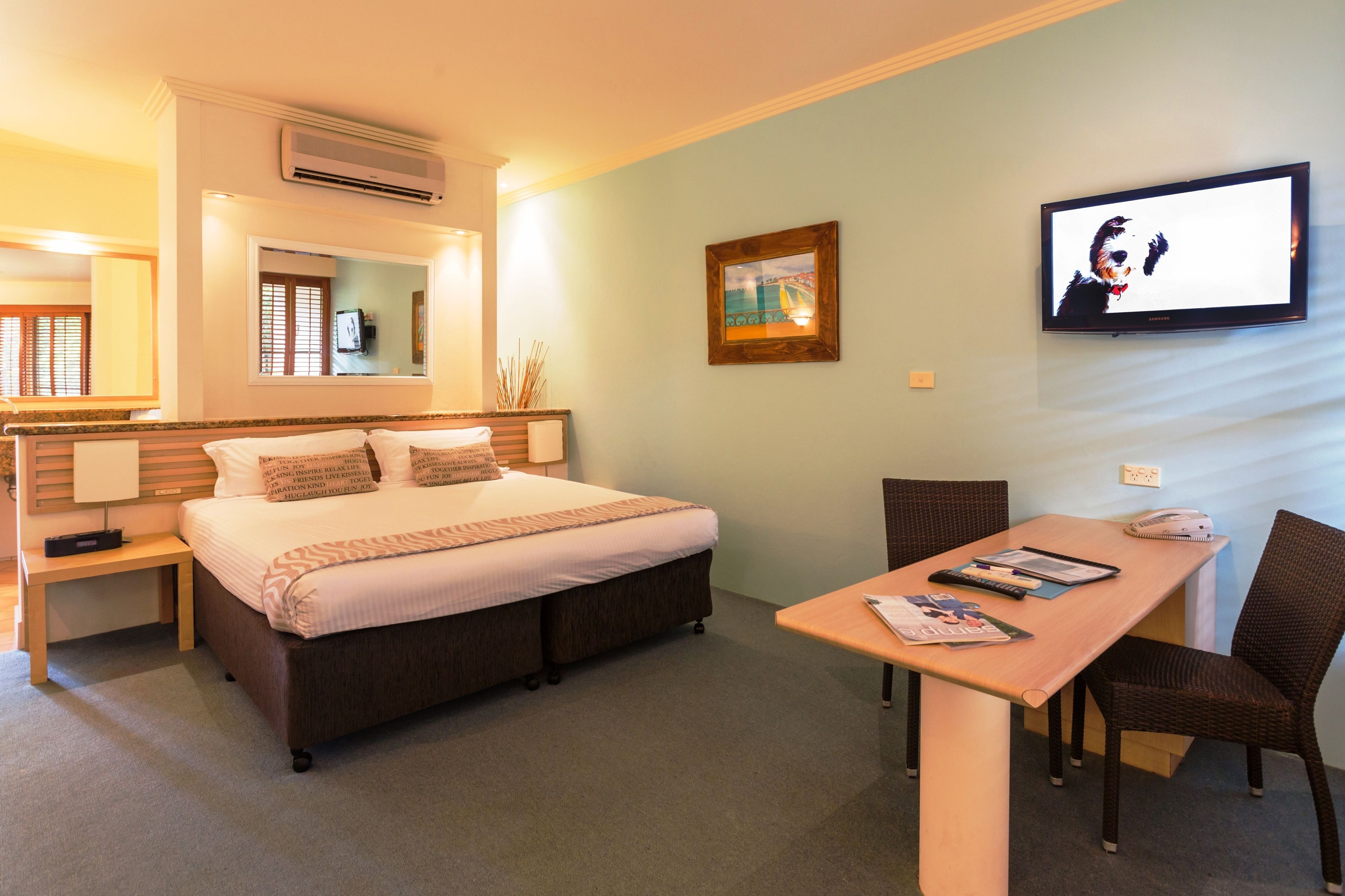 A hotel room with a bed, a desk with a chair, a television, and a painting on the wall.