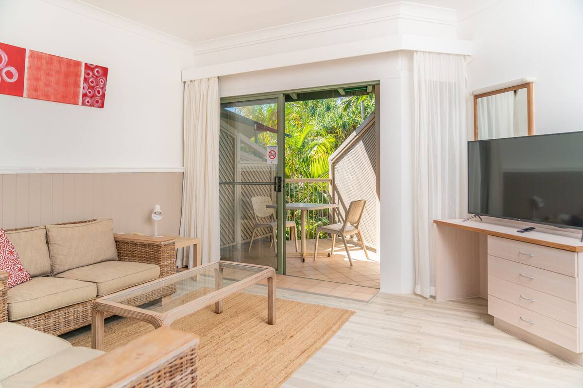 A modern living room with a sofa, coffee table, TV, and a sliding glass door leading to an outdoor area with a table and chairs.