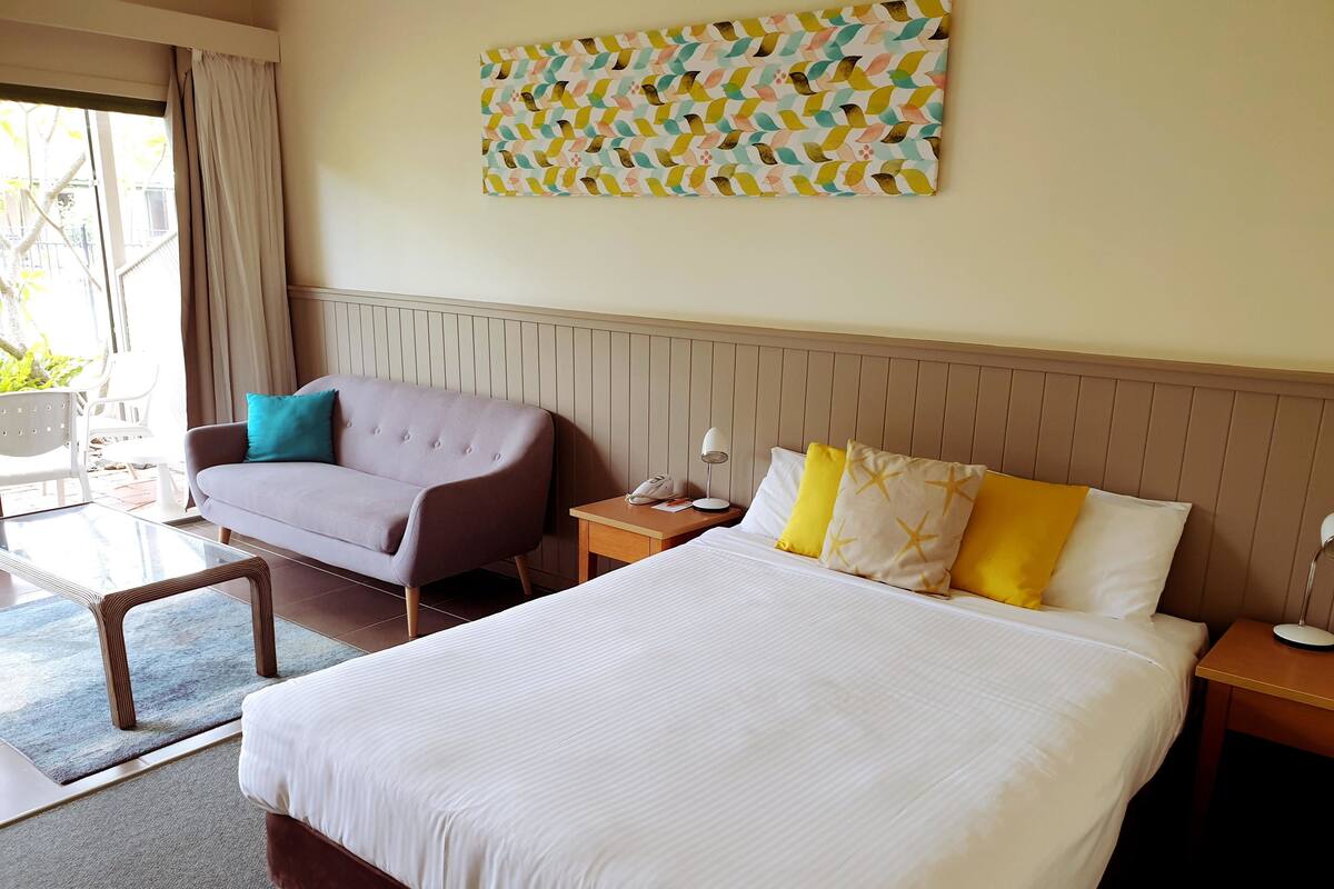 A hotel room with a large bed, a sofa, a small table, and a nightstand.