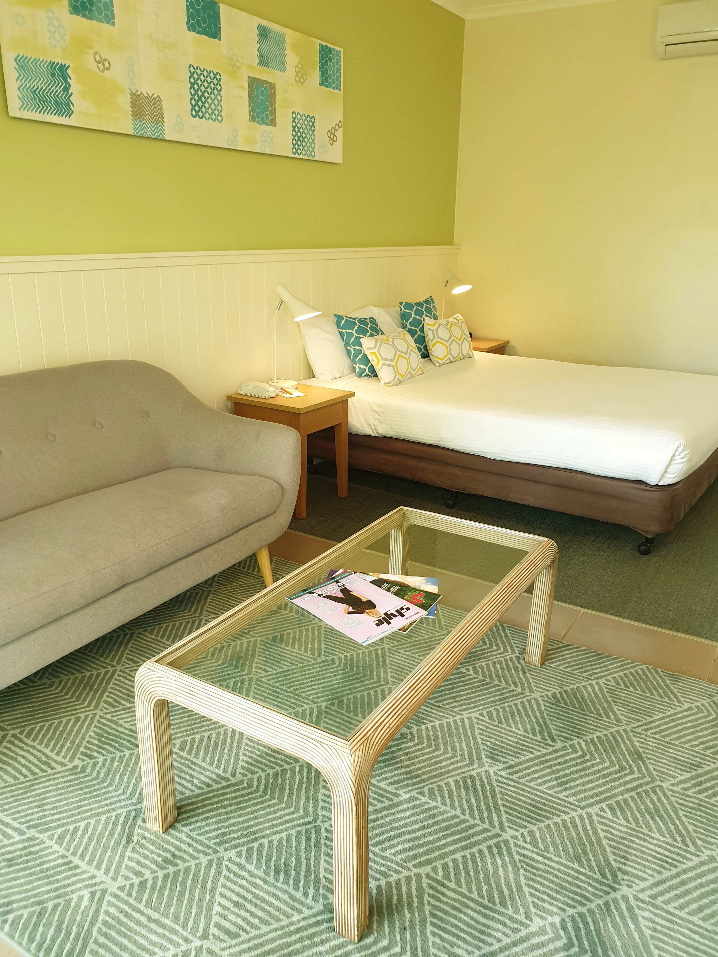 A room with a bed, a sofa, a small table, and a wall with a geometric pattern.