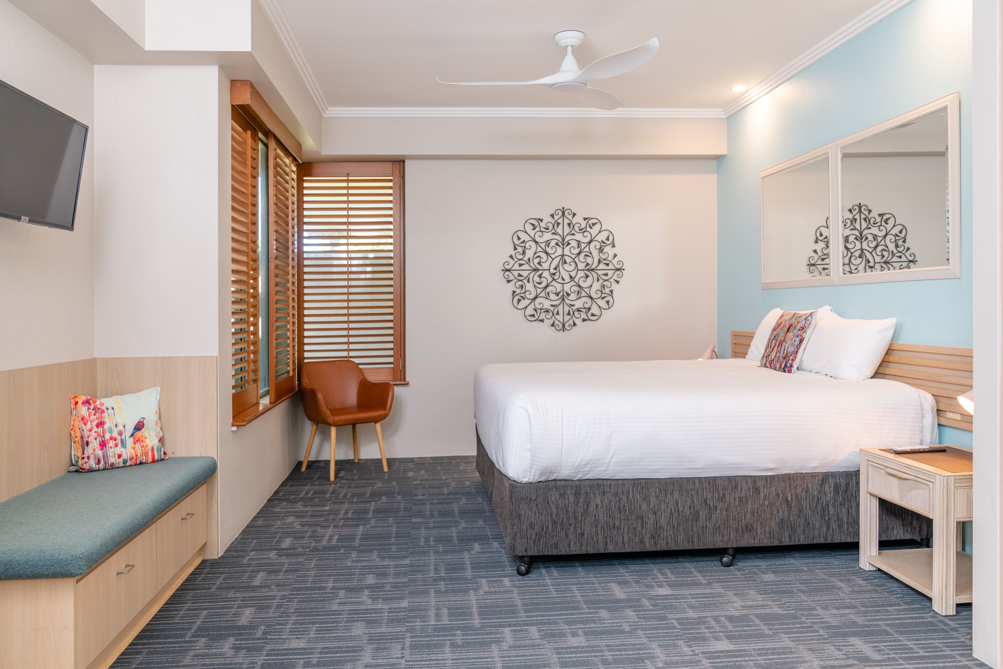 Habitación de hotel con cama, escritorio, silla, televisor y un elemento decorativo en la pared.