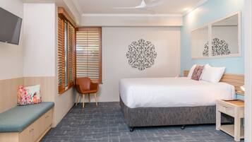 A hotel room with a bed, a desk, a chair, a TV, and a decorative wall piece.