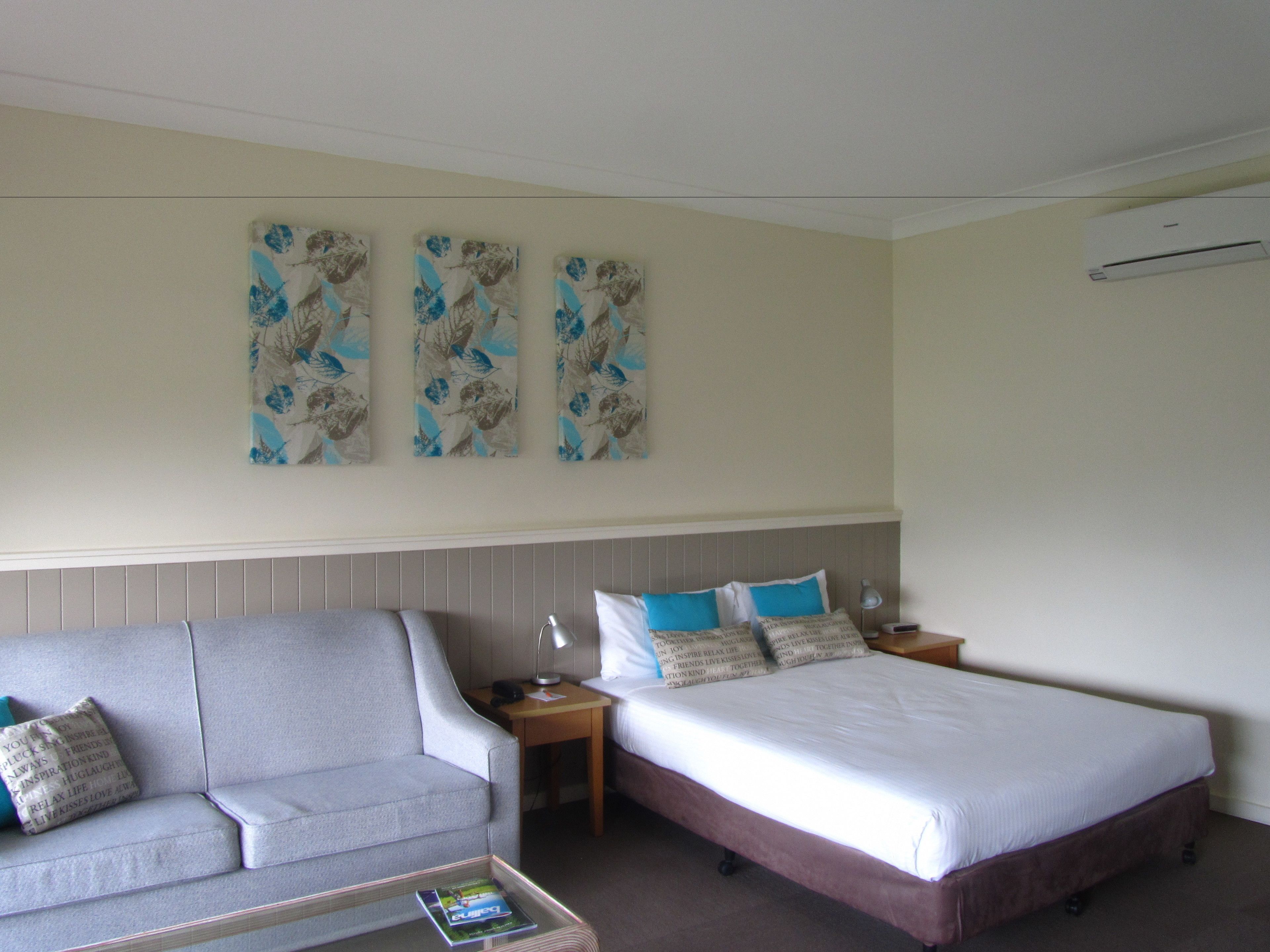 A hotel room with a bed, a sofa, and a small table. There are three wall art pieces above the bed.