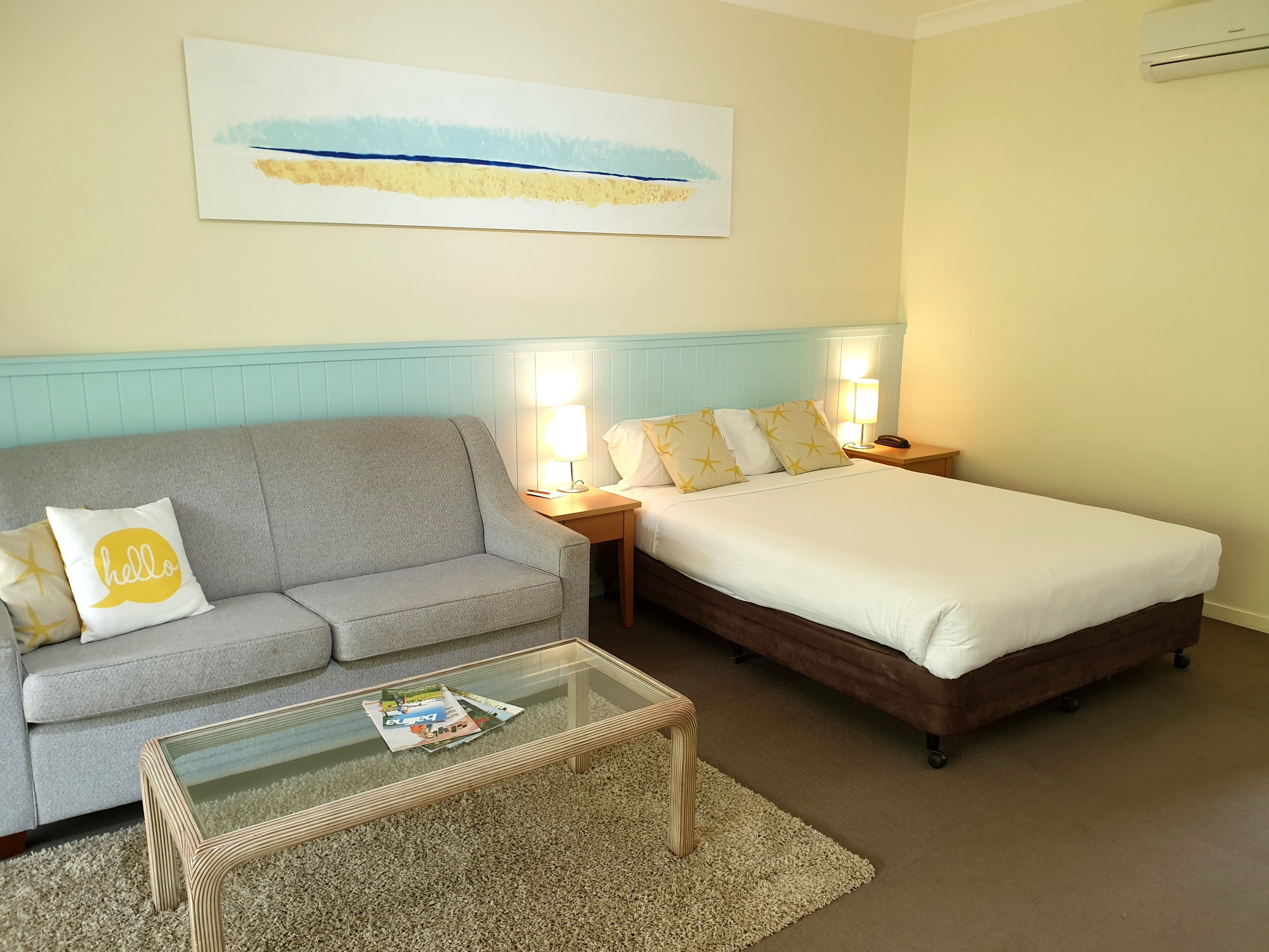 Ein Hotelzimmer mit grauem Sofa, einem Bett mit weißer Bettwäsche und einem Glastisch.