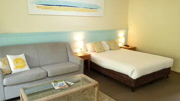 Una habitación de hotel con un sofá gris, una cama con ropa de cama blanca y una mesa de centro de vidrio.