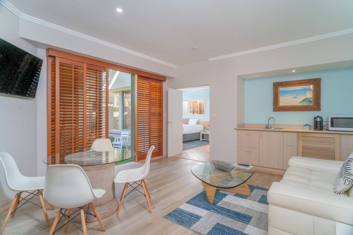 A modern living room with a glass coffee table, white sofa, and a dining area with a glass table and chairs.