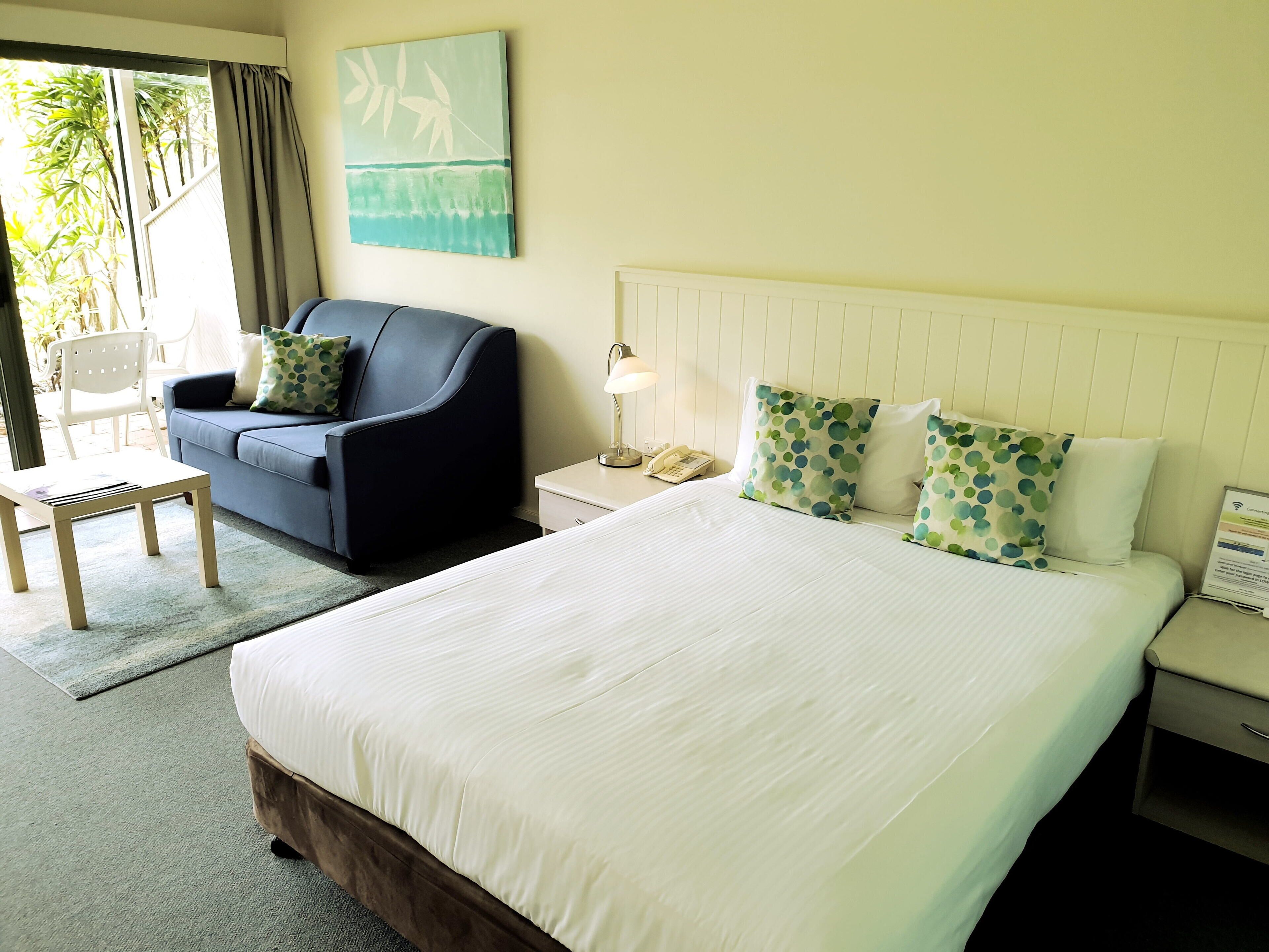 A hotel room with a large bed, a sofa, a chair, and a painting on the wall.