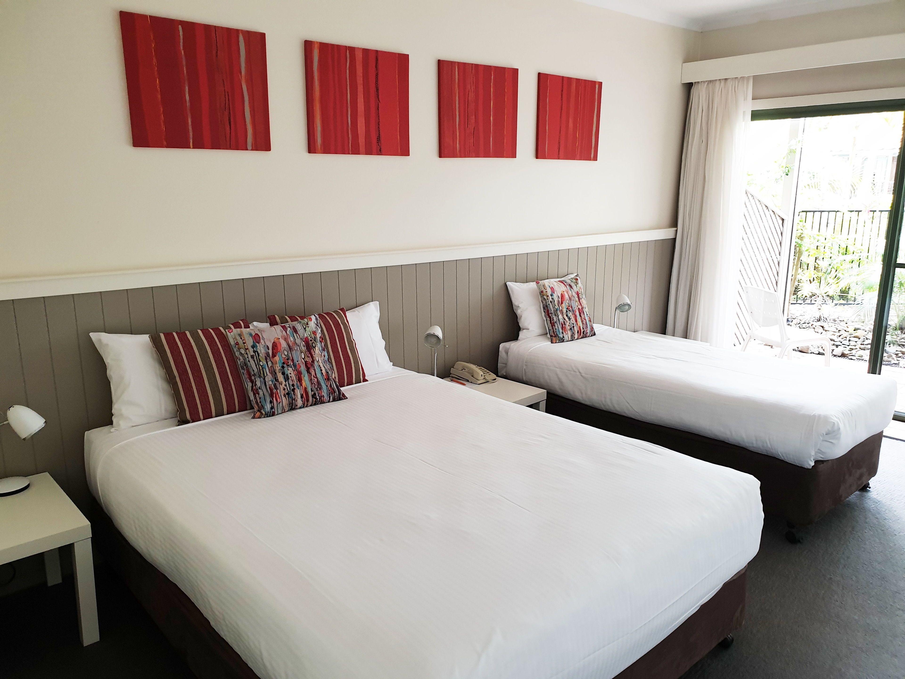 Une chambre d’hôtel avec deux lits, une petite table, une lampe de chevet et une fenêtre donnant sur l’extérieur.