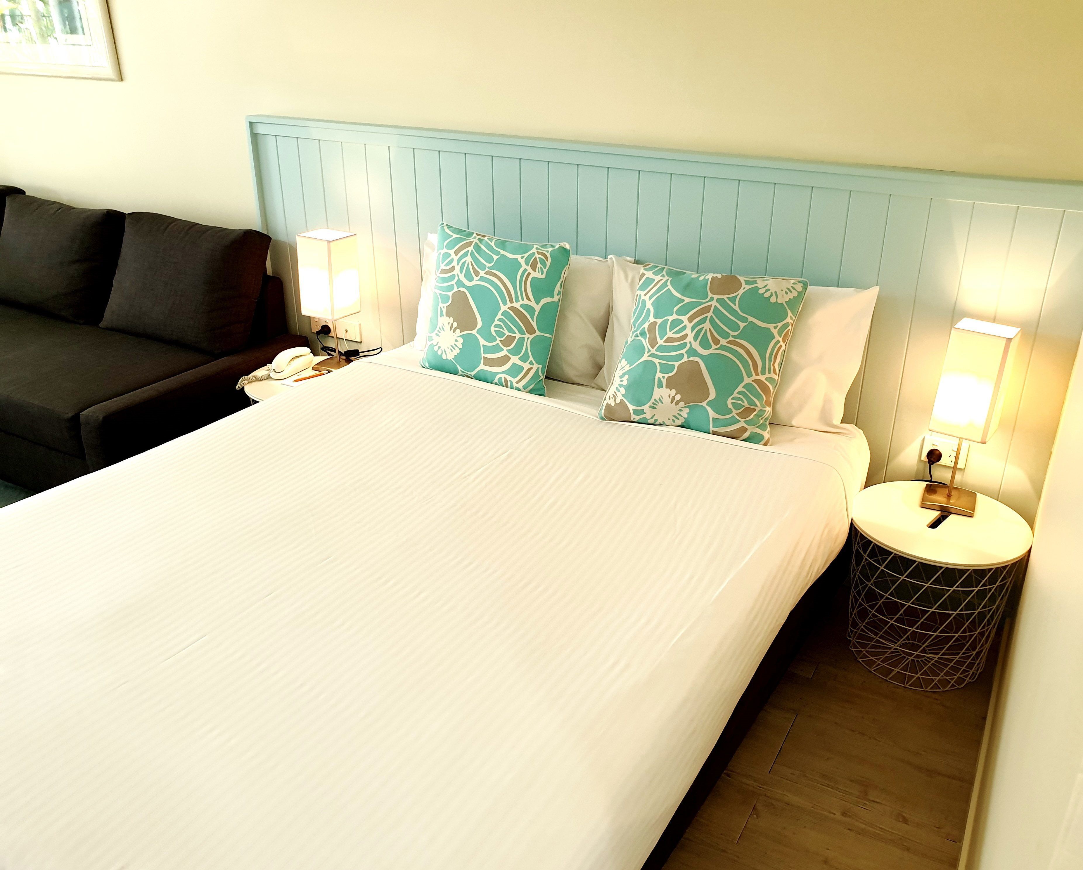 A hotel room with a large bed, two bedside lamps, a nightstand, a telephone, and a dark-colored sofa.
