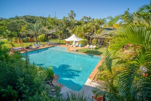Une piscine entourée d’une végétation luxuriante et de palmiers, avec des chaises longues et un kiosque.