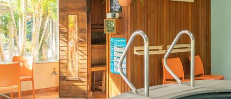 A wooden spa area with a hot tub, wooden walls, and a window overlooking palm trees.