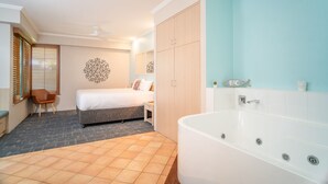 Ein Hotelzimmer mit Bett, Sitzgelegenheit, einer großzügigen Badewanne und einem Kleiderschrank.