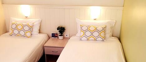 A hotel room with two beds, each with a white bedspread and matching pillows. There are three framed pictures on the wall above the beds.