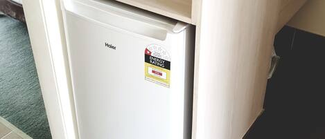 Un refrigerador compacto con un microondas encima, una etiqueta visible de eficiencia energética y un pequeño área de lavamanos a la derecha.
