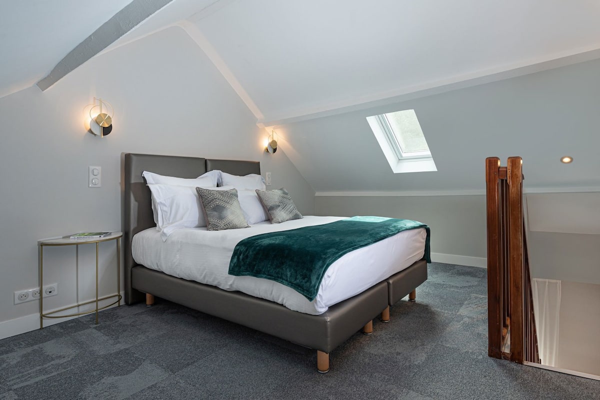 Un dormitorio moderno con tragaluz, cama con manta verde y mesita de noche.