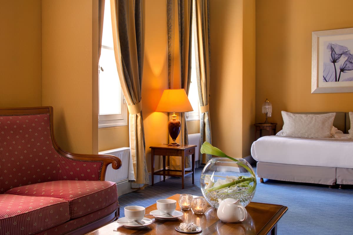 Habitación de hotel con sofá rojo, cama blanca, una mesa con juego de té y un acuario.