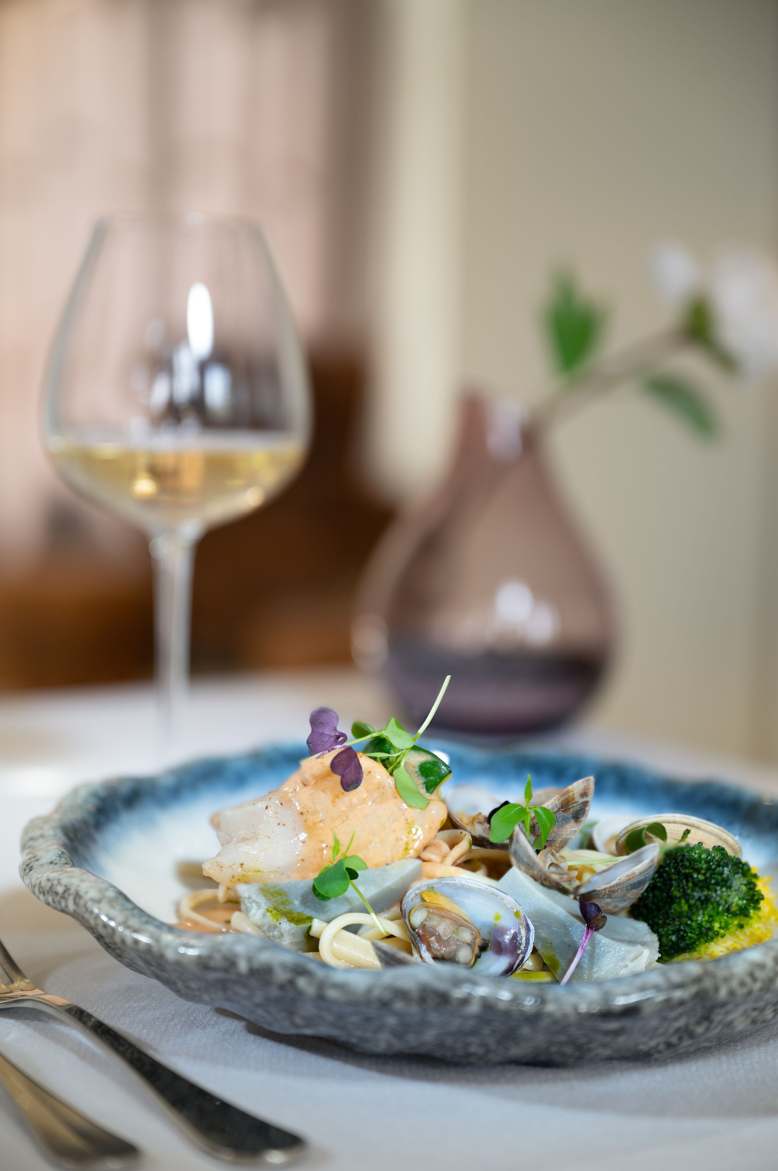 Prato de comida com um copo de vinho branco ao fundo.