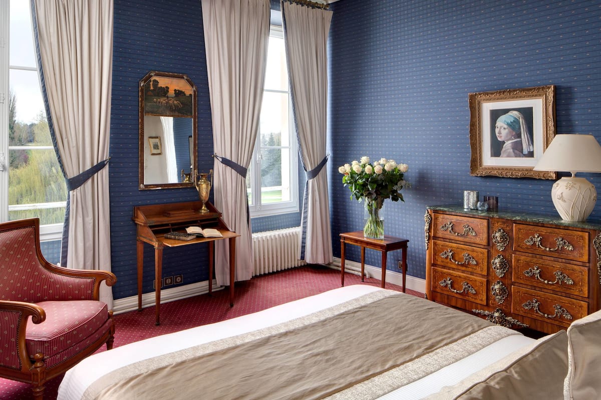 Un dormitorio con una cama grande, un aparador de madera, un espejo y una ventana con cortinas.