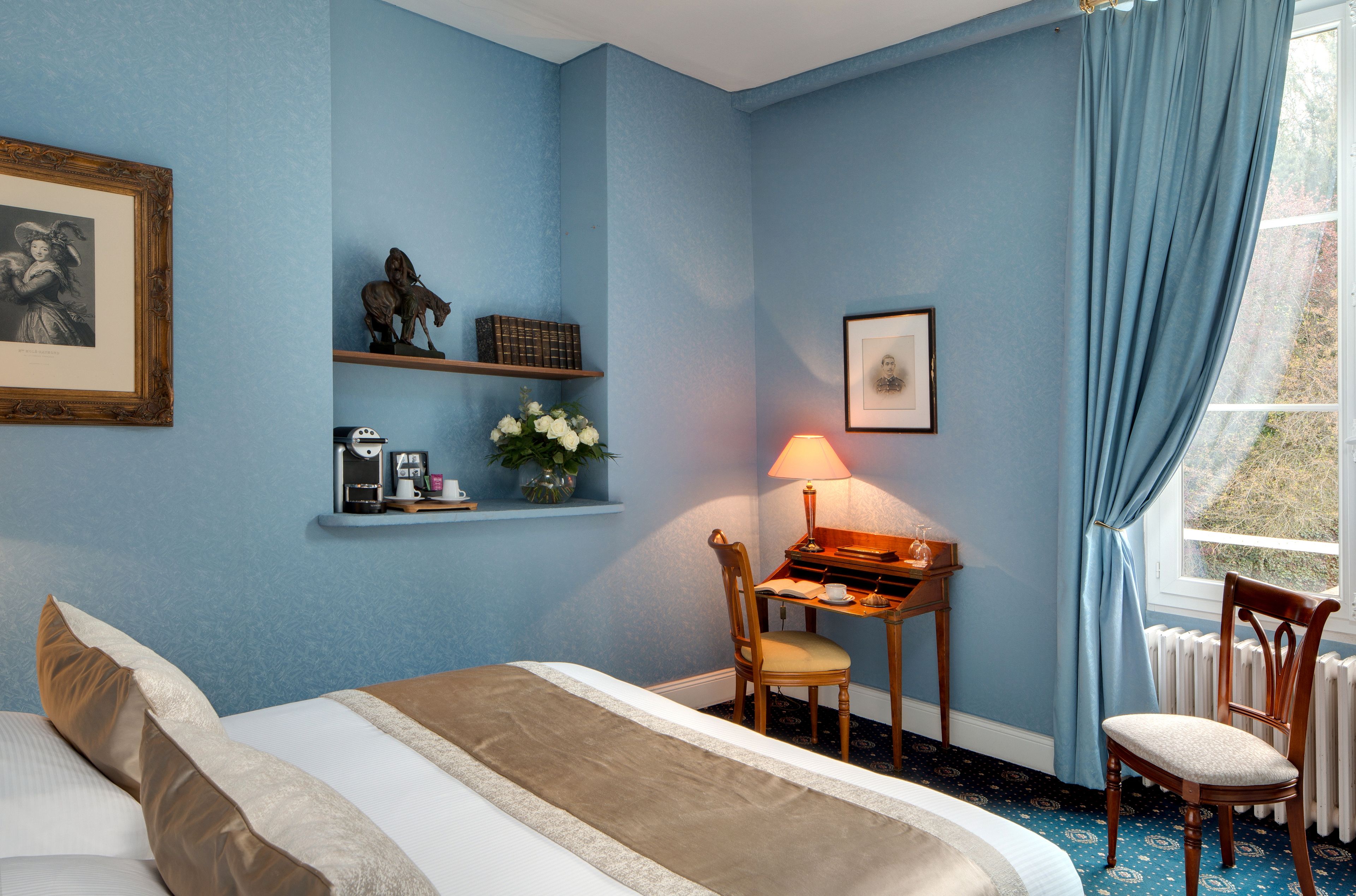 A bedroom with a bed, a desk with a lamp, a chair, a shelf with decorative items, and a window with curtains.