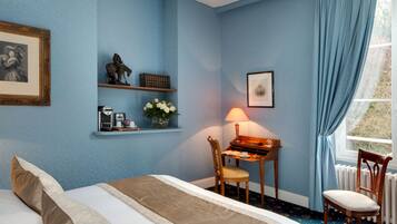A bedroom with a bed, a desk with a lamp, a chair, a shelf with decorative items, and a window with curtains.